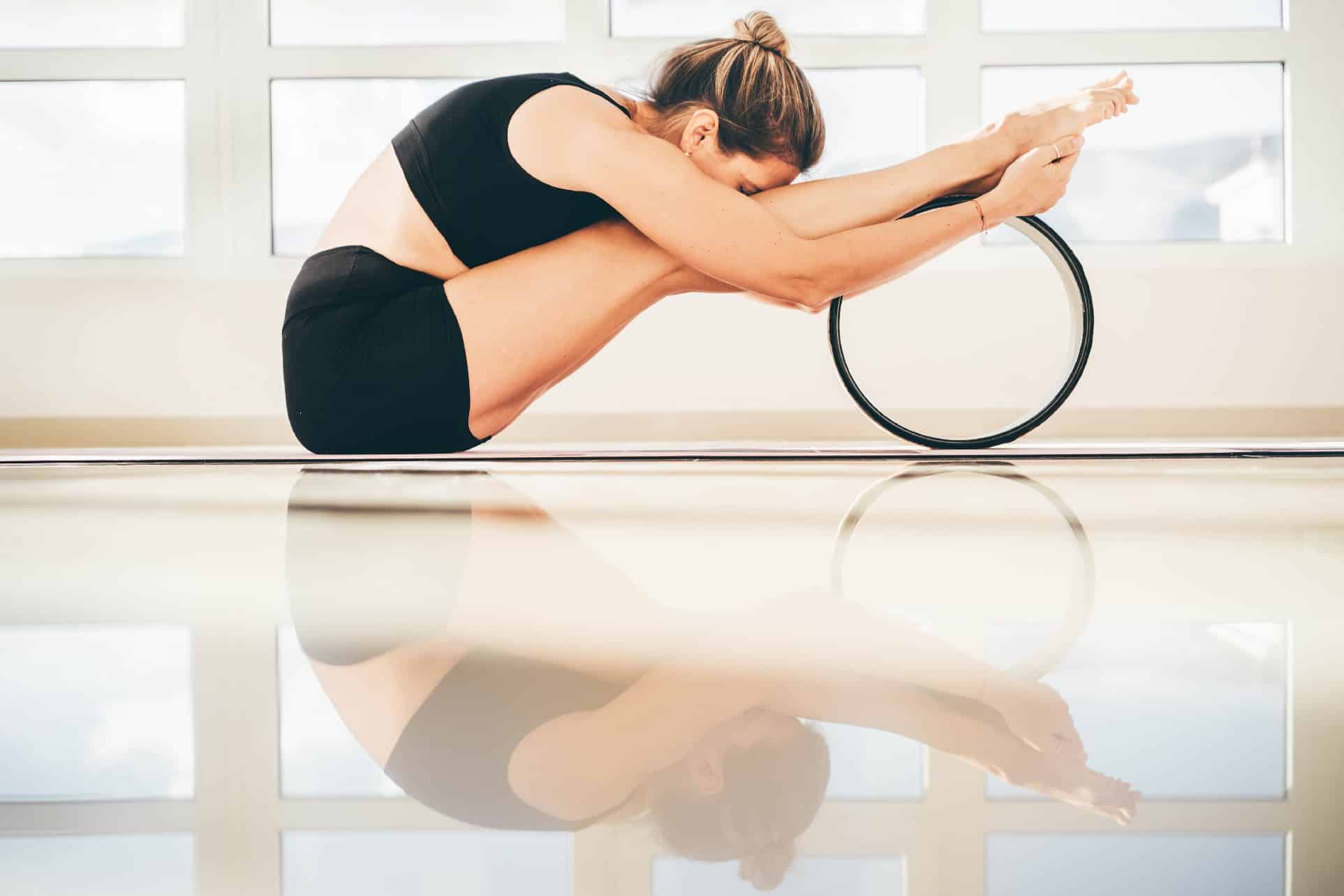 Sportive woman training using yoga wheel to build spine and back flexibility.